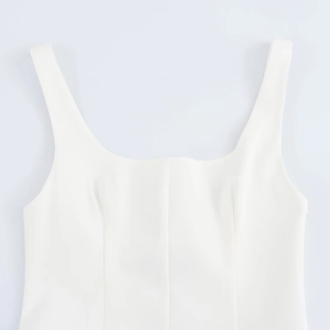 Detail of square neckline and structured seams on a white sleeveless dress with wide straps