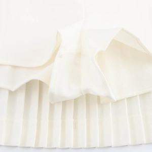 Close-up of pleated white mini dress hem featuring neat stitching and woven fabric