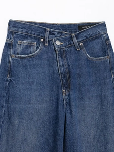 Détail d'un jean bleu foncé à taille haute avec une ceinture asymétrique superposée unique