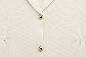 Détail du haut en tricot crème avec des boutons métalliques dorés de forme irrégulière