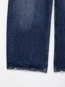 Gros plan détaillé du jean bleu foncé montrant les coutures jaunes et la texture de l'ourlet