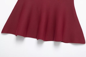 Close-up of wine red knit dress hem showing detailed ribbed texture and draped fabric edge