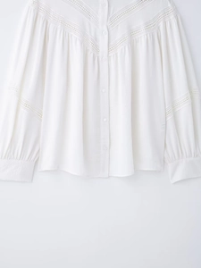 Detailed view of V-shaped lace embroidery and button closure on white cotton shirt