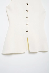 Détail du gilet en maille blanche avec boutons dorés décoratifs et fente sur l'ourlet bas