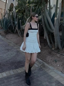 Detailed view of the white mini dress with black straps and bubble hem in outdoor setting