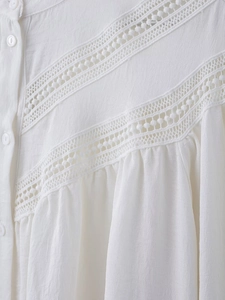 Detail of white blouse with V-shaped hollow lace stitching and round button closure