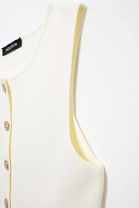 Détail du gilet en maille blanche avec boutons dorés et étiquette de marque au col