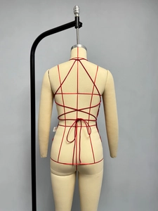 Detail of red strappy body harness with geometric cross-back design and waist bow tie