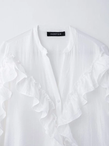 Dettaglio della camicia bianca a maniche lunghe con volant sulle spalle e colletto alla coreana