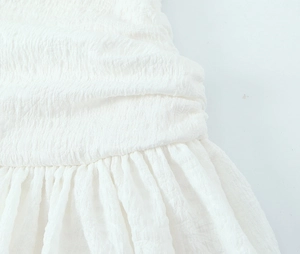 Detail of white balloon dress featuring pleated texture and ruffle hemline on fabric