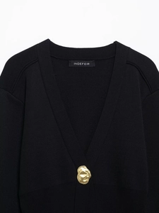 Macro view of black knit cardigan with artistic gold metal button and brand neck label