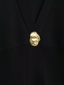 Close-up of black knit fabric with a unique molten gold metal buckle detail