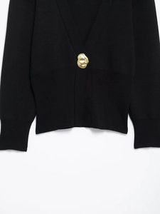 Detail of black knit cardigan featuring a textured fabric and a unique gold metal button