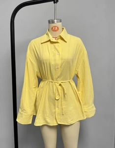 Detail of yellow long-sleeved shirt featuring textured fabric and adjustable waist tie