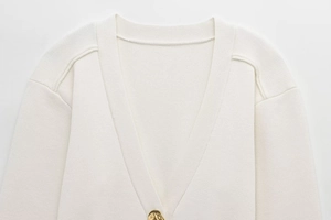 Detailed close-up of cream knit cardigan with V-neckline and premium gold geometric button