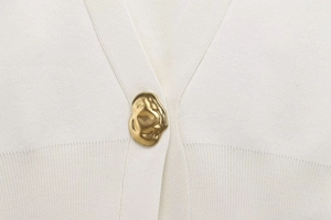 Close-up of white fine knit cardigan with a textured gold irregular metal button