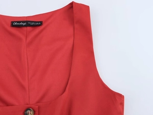 Close-up of red vest top featuring a square neckline, brand label, and tortoiseshell button