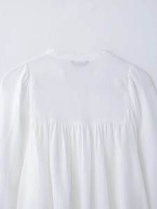 Detailed close-up of white blouse featuring elegant back pleats and vertical texture