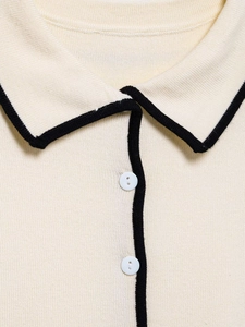 Close-up of cream knit polo top with black contrast trim and white button details