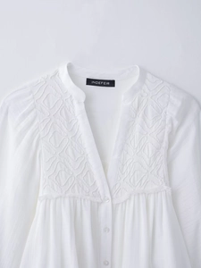 Close-up of white long sleeve shirt showing delicate geometric embroidery and V-neck detail