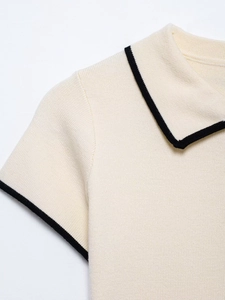 Detail of cream knit polo shirt featuring refined black contrast piping and soft texture