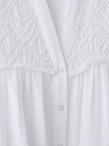 Close-up of white cotton linen shirt featuring geometric embroidery and tassel details