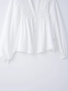 Detail of elegant white long sleeve blouse featuring intricate hollow embroidery and buttons