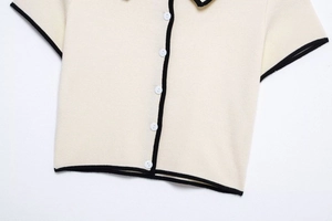Close-up of cream short-sleeve knit cardigan with black contrast trim and buttons