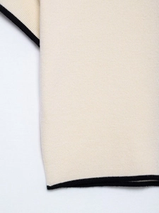 Detailed close-up of cream knit fabric with contrasting black braided edge trim