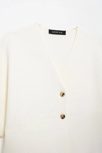 Close-up of cream knit top featuring a V-neckline and two decorative gold metallic buttons