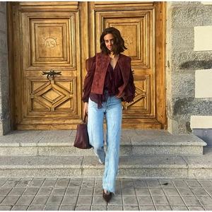 Detail of vintage burgundy embroidered vest styled with layered ruffle blouse and jeans