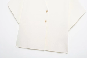 Detail of creamy white vest featuring two golden round metal buttons and fine fabric texture