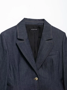 Détail d'un blazer en jean bleu marine avec revers crantés et bouton en métal doré