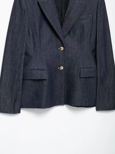 Vue détaillée du blazer en jean bleu foncé avec revers à pointe et boutons dorés