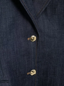 Gros plan d'une veste en jean bleu foncé avec surpiqûres et boutons dorés martelés