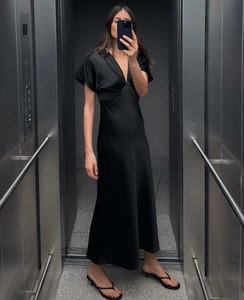 Détail d'une élégante robe longue en satin noir avec col en V profond et manches volantées