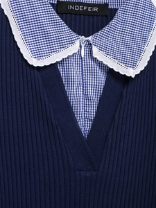 Dettaglio di top blu in maglia con colletto a quadri, pizzo bianco e zip sulla scollatura