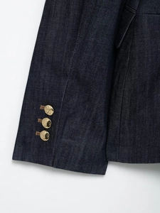 Détail de manches de blazer en jean bleu marine avec boutons dorés texturés et denim