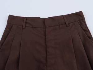 Detail of high waist pleated brown trousers featuring belt loops and seamless zip fly