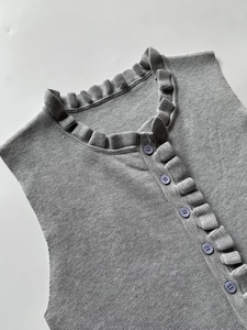 Detail of grey knit vest with ruffled crew neck and contrasting purple buttons