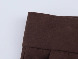 Detail of dark brown pleated trousers showing wide elastic waistband and fabric texture