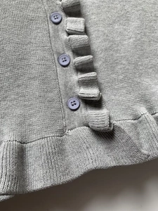 Detail view of light grey knit top featuring delicate ruffles and lilac button accents