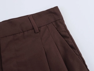 Detailed close-up of dark brown pleated trousers featuring waist loops and twill texture