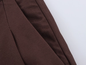 Detail shot of pleated brown trousers showing the side pocket and fine stitching texture