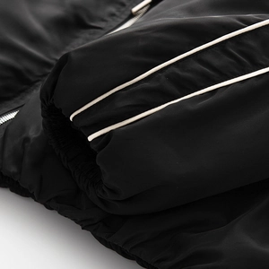 Détails de veste bomber noire avec rayures blanches et finitions de poignets élastiques