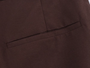 Detail view of the rear welt pocket and twill texture on chocolate brown pleated trousers