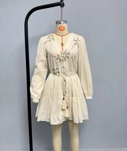 Detailed close-up of bohemian floral embroidery and tassel drawstring on a beige dress