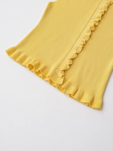 Close-up of vibrant yellow ribbed knit fabric with delicate ruffle trim and small round buttons