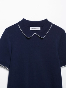 Détail d'un haut en tricot bleu marine avec bordure festonnée blanche au col et manches