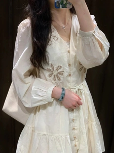 Detail of cream long sleeve dress featuring brown floral embroidery and wooden buttons